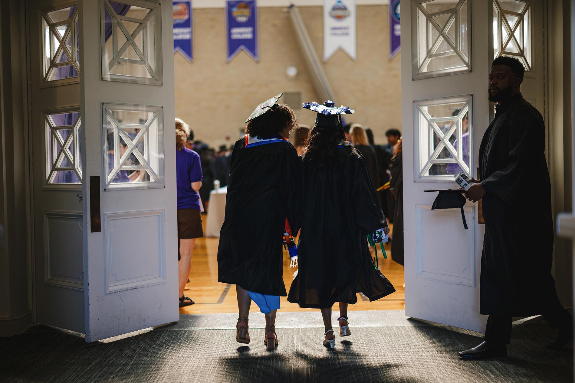 Two graduates in silouhette from behind entering the Alumni Gym.