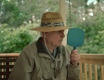 An old man wearing a hat looking into a handheld mirror