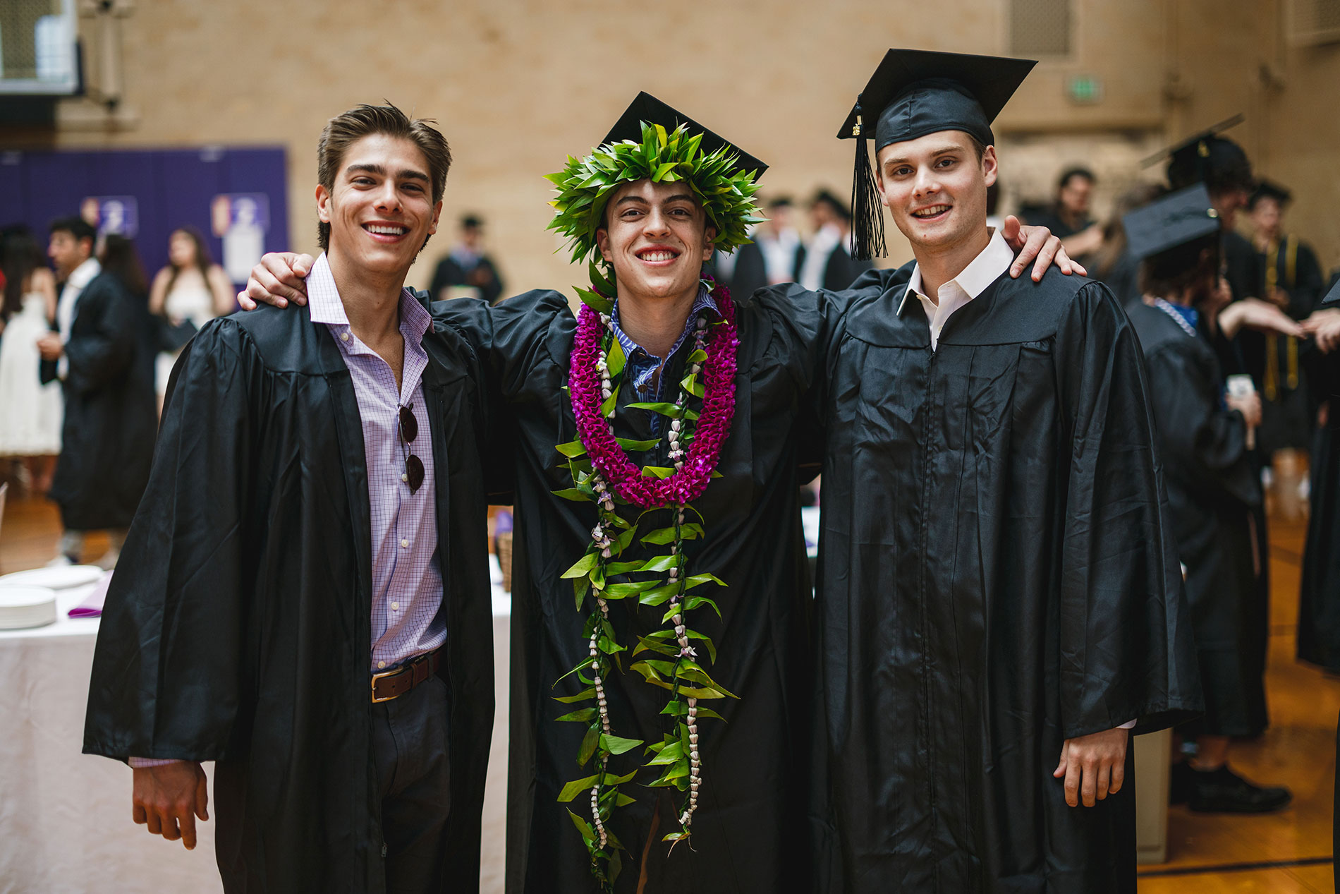 Three young men in graduation gowns and caps, and one with a leafy wreath on his head.
