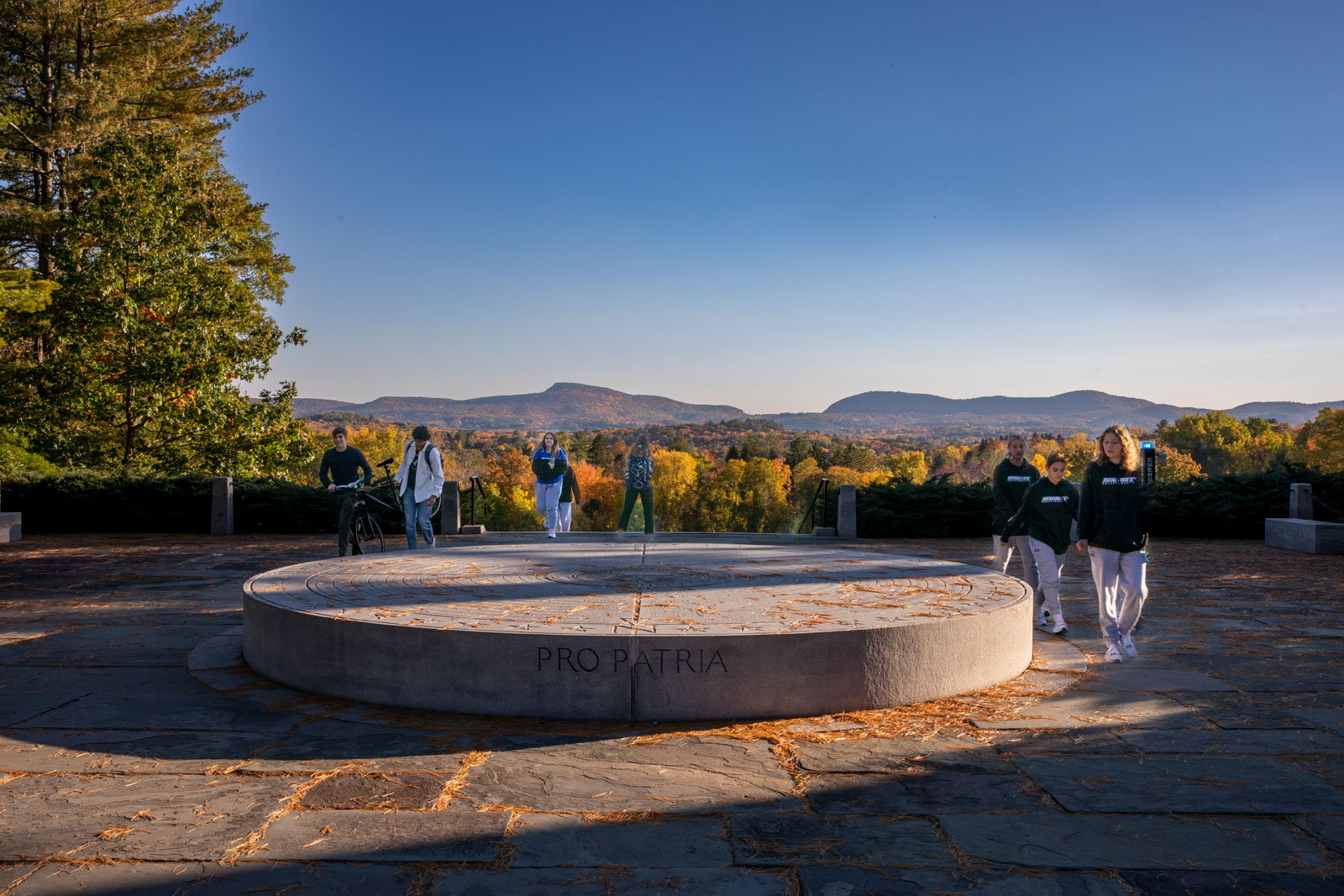 students walk around the war memorial with mountains in the distance in autumn at sunset