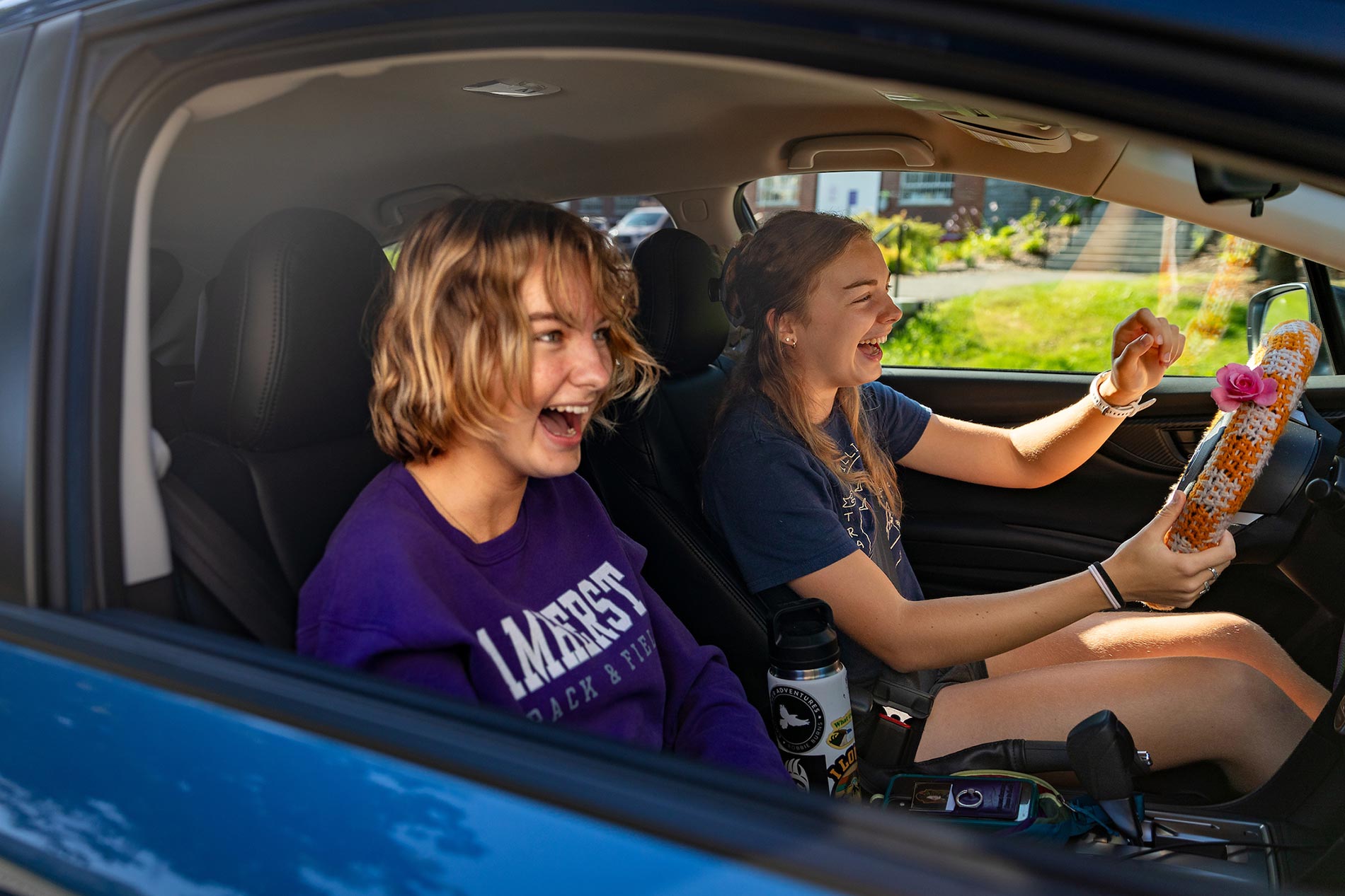 Two young women in laugh while sitting in the front seat of a car.