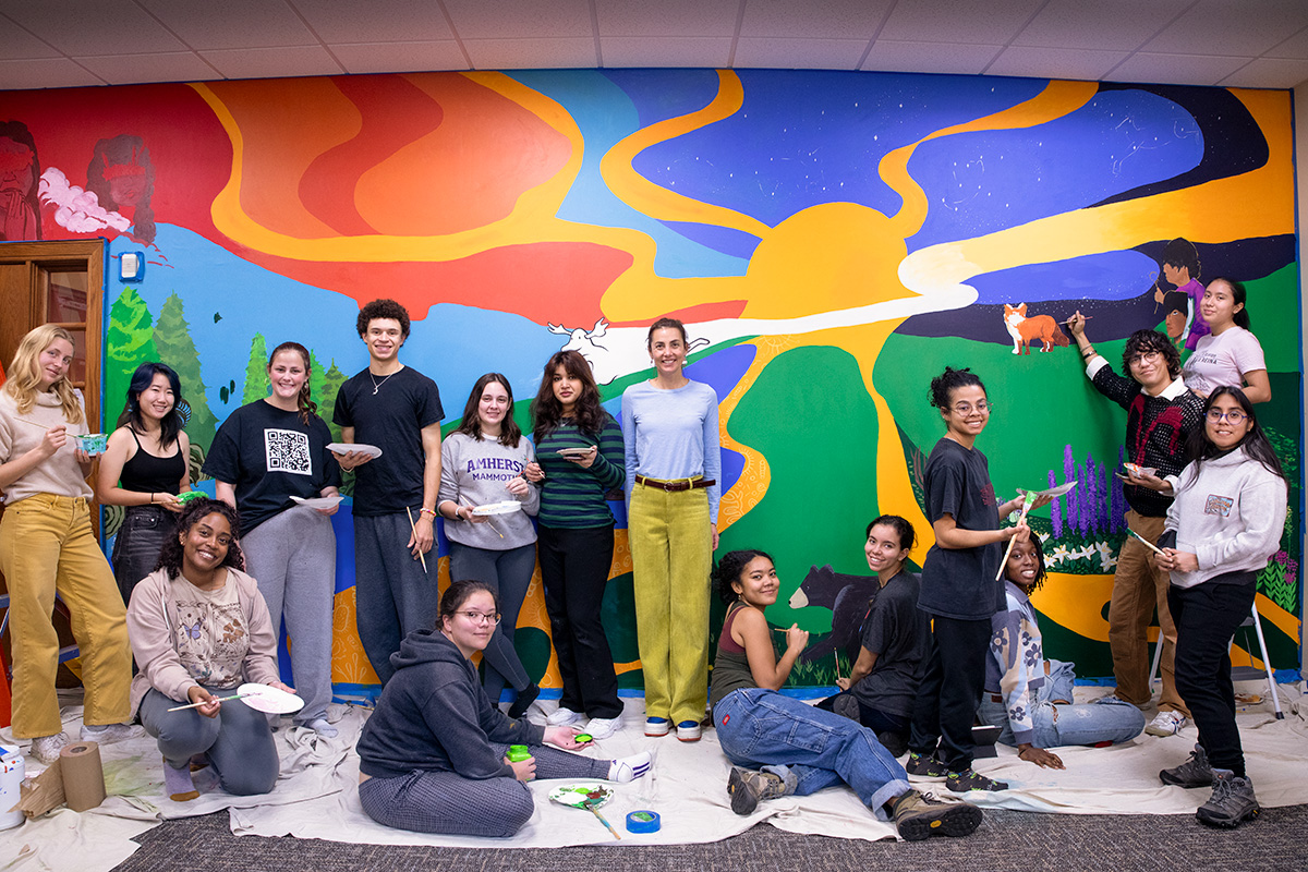 A group of students with paintbrushes in front of a colorful mural