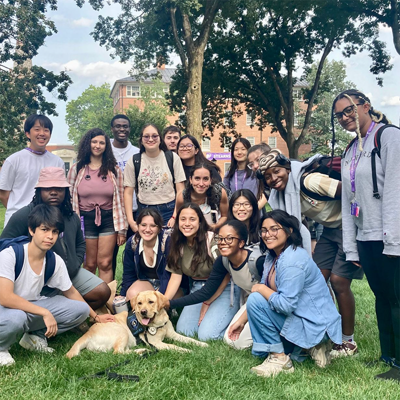 Students poising outside around a dog sitting in the grass