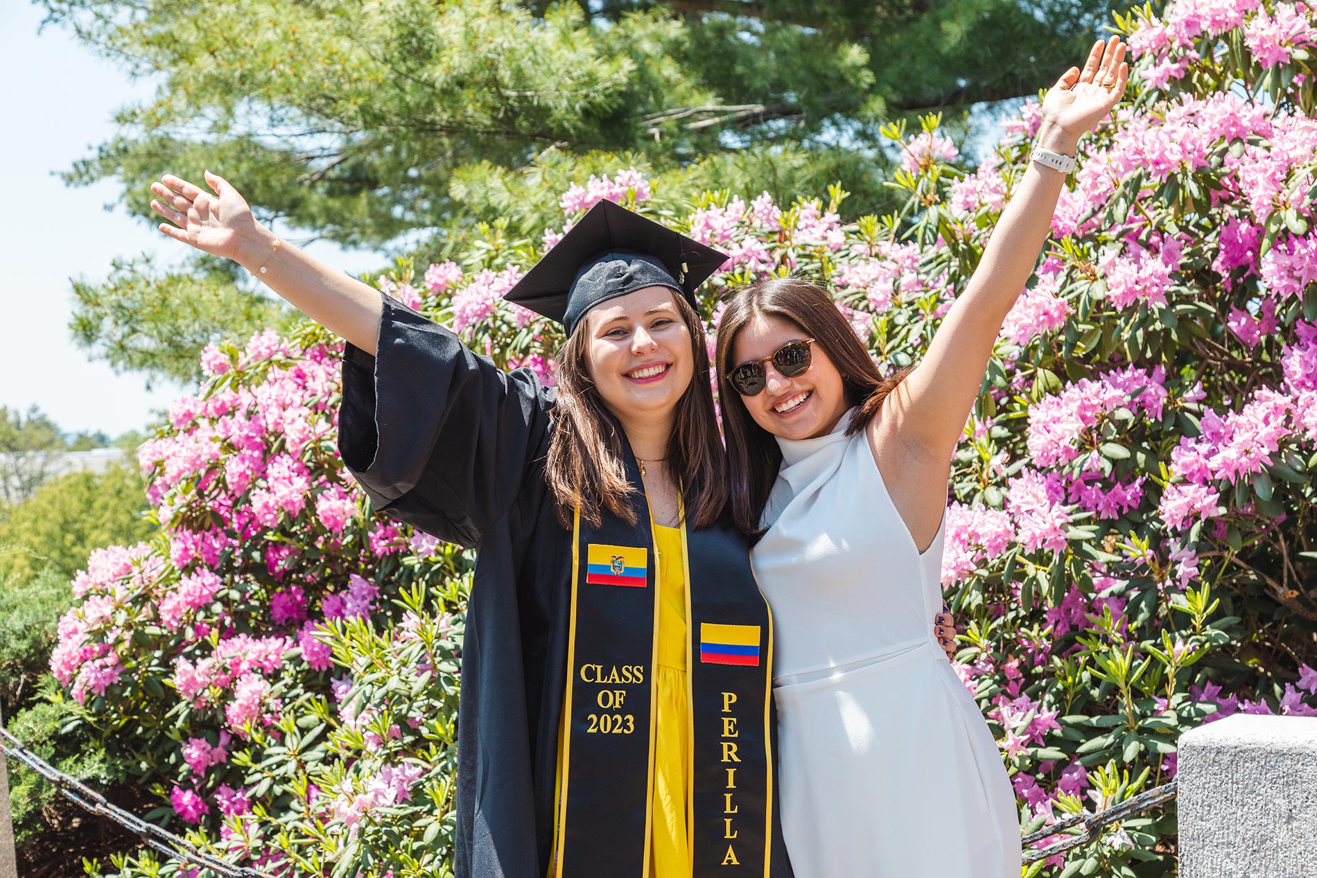 A graduate and her family member raise their arms in celebration.