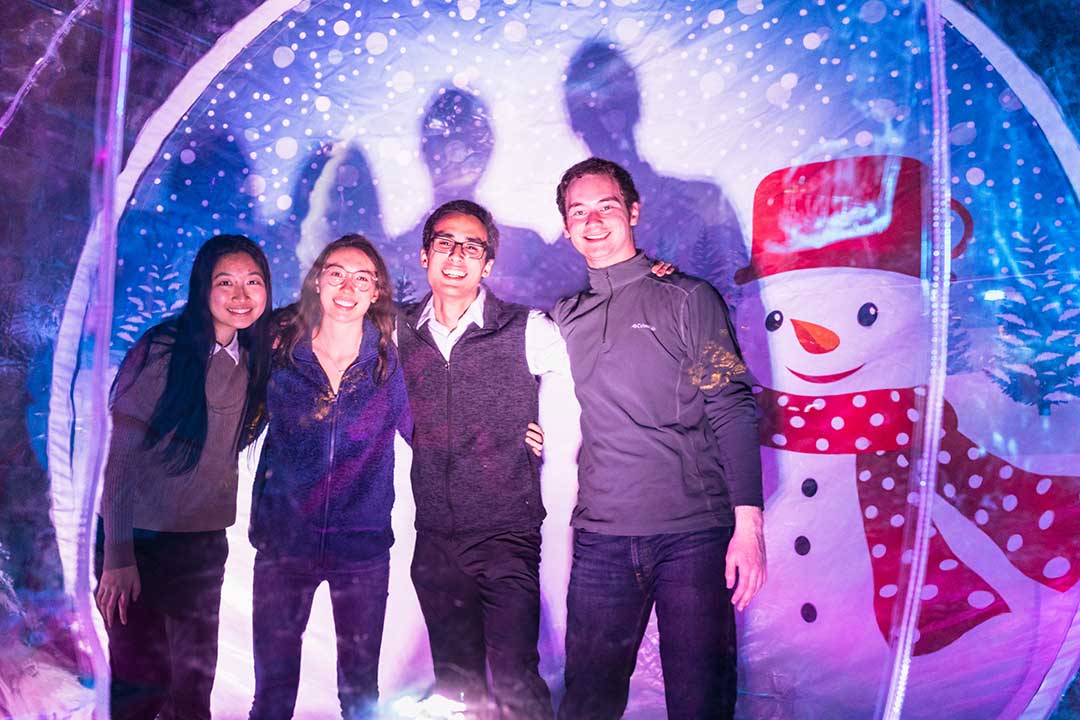 Four college students pose for a photo inside a giant blow up snow globe.