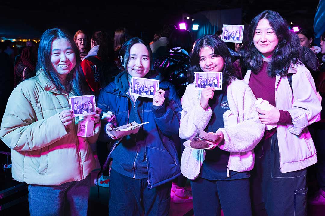 Four young women, balancing plates of food, hold up copies of a photo of the four of them from the Winter Fest photo booth.