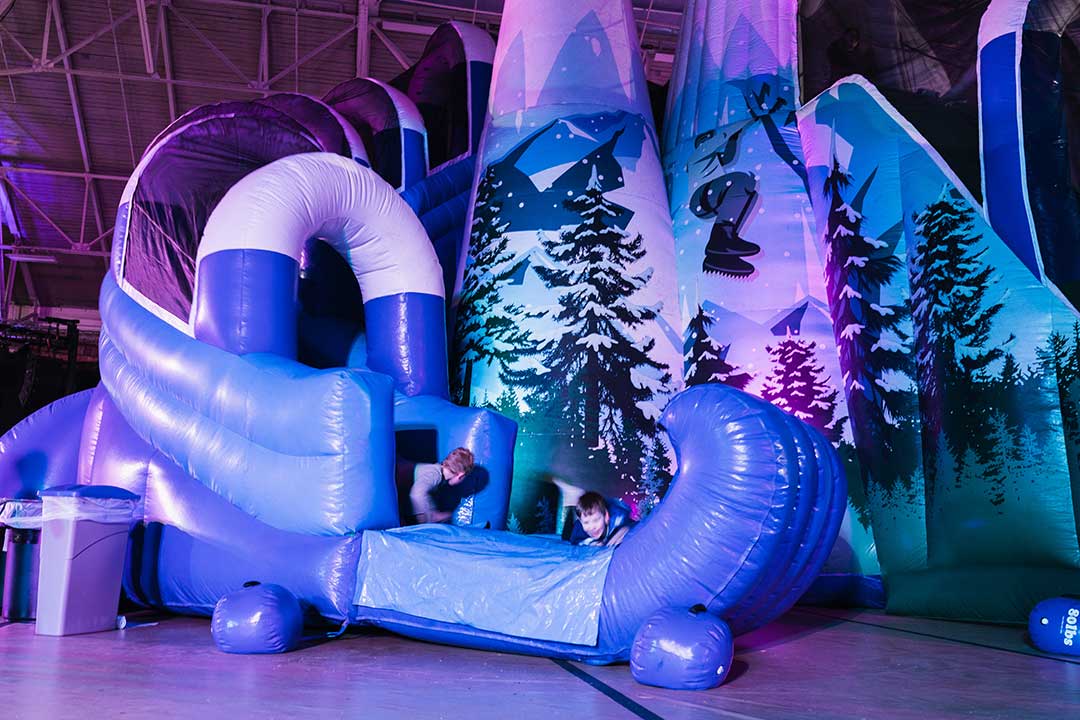 Two children play inside a large blow up blue and purple slide.