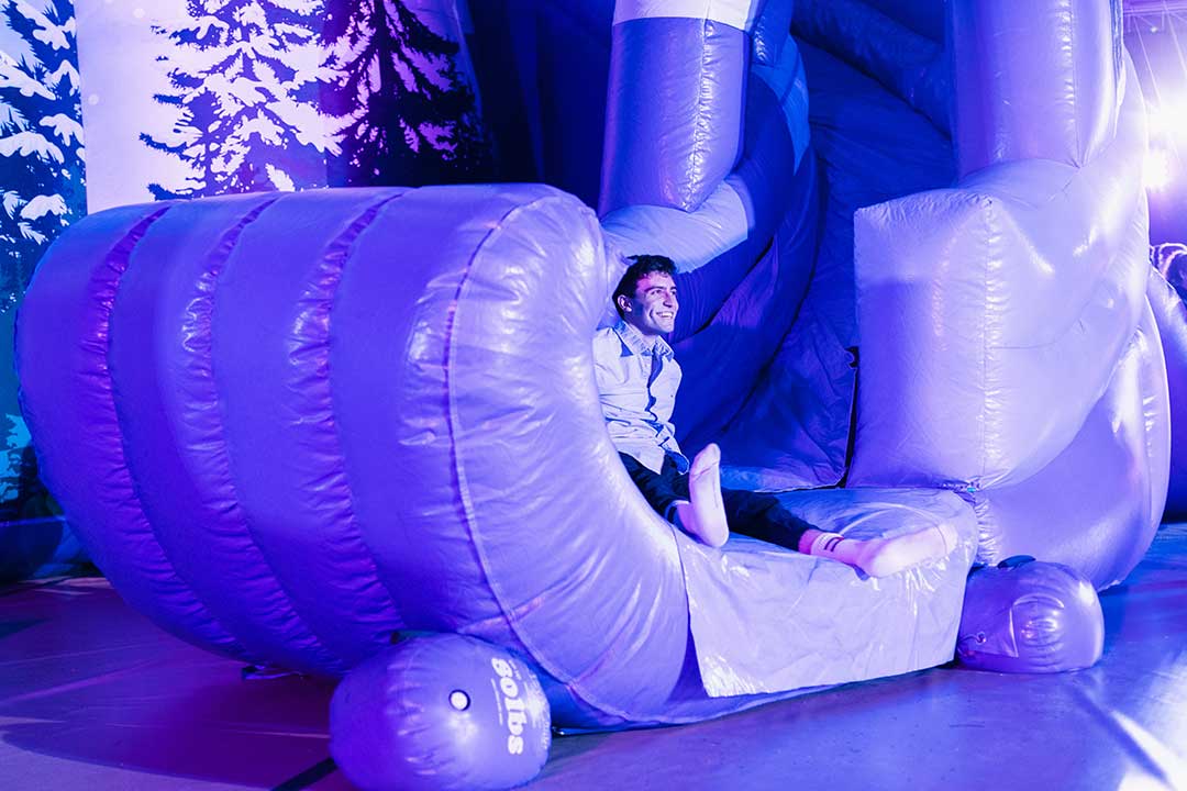 A young man appears at the bottom of a large blow up indoor slide.