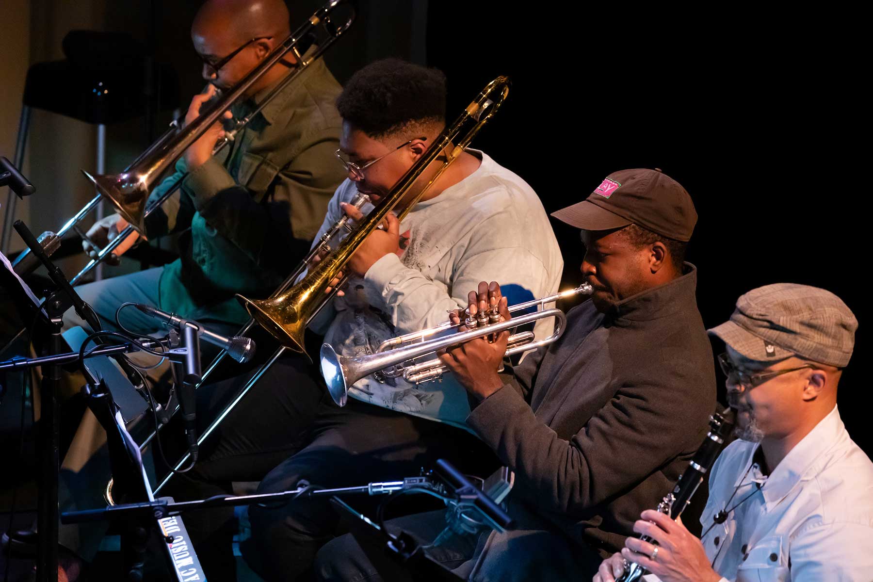 Four men sitting in a line on stage playing wind instruments.