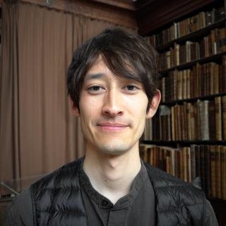 Headshot of Toma-Jin Morikawa-Fouquet in front of a bookshelf